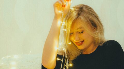 a woman sitting on a bed holding a string of lights